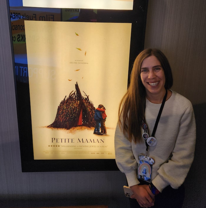 a photo of SLFS Staff member Ally Lantz standing next to a movie theater poster for Petite Maman