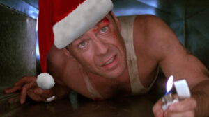 A beat up man in a Santa hat with a lighter crawls through a tight space.